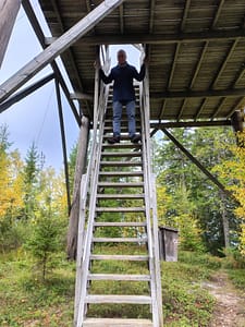 Man standing at the top of a wooden tower ladder.