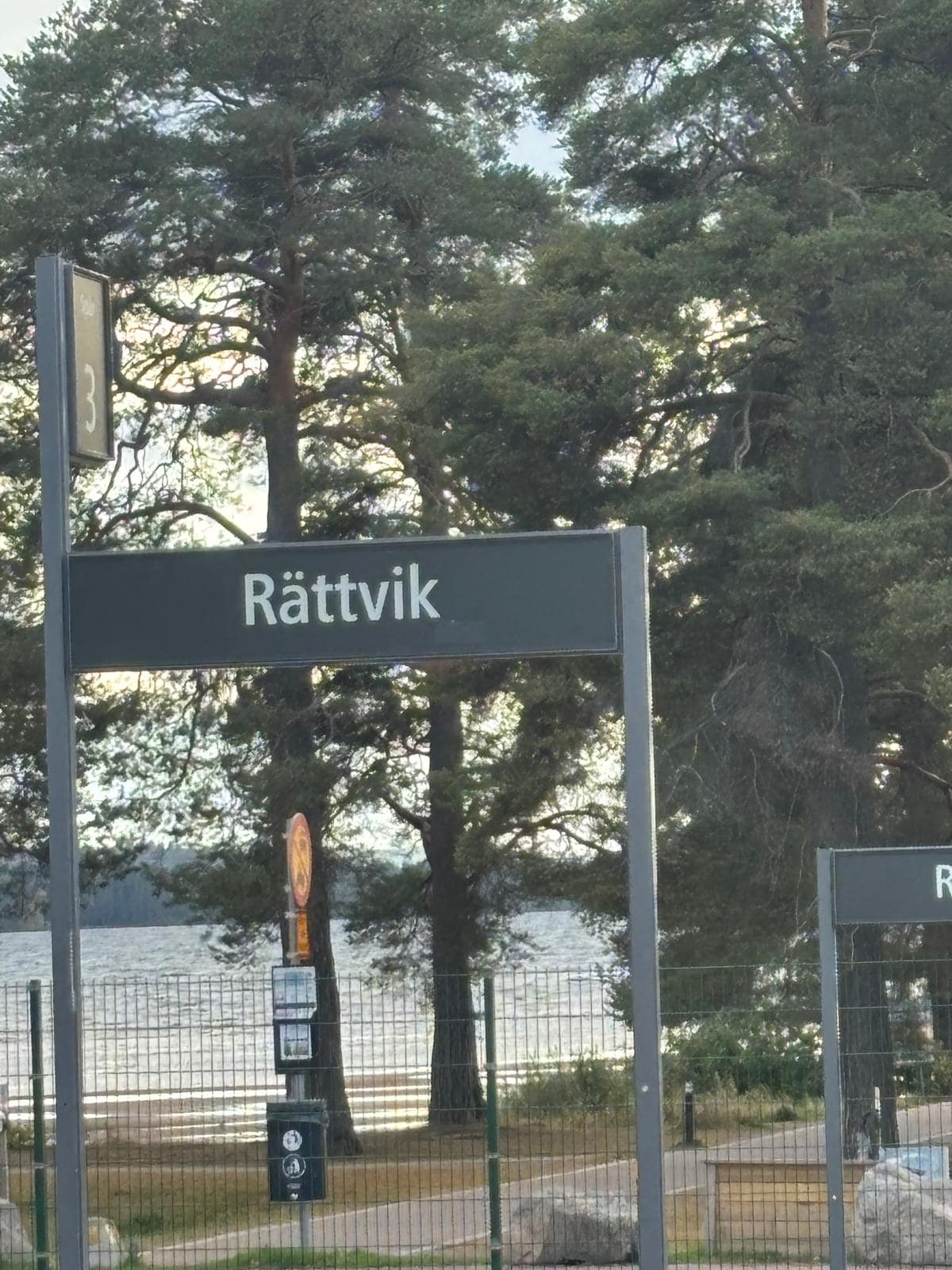 Train station sign for Rättvik with lake and trees.