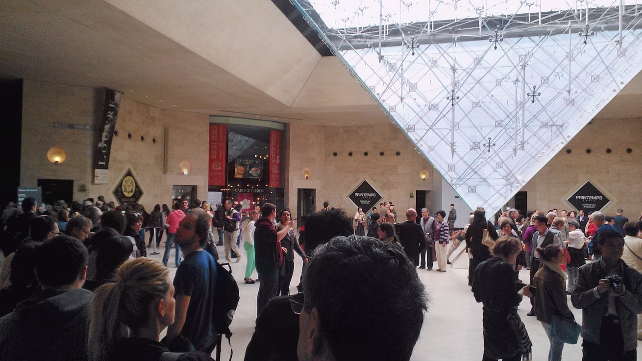 En stor folksamling och turister under den omvända glaspyramiden i Carrousel du Louvre i Paris, som visar urban trängsel