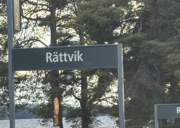 Train station sign for Rättvik with lake and trees.